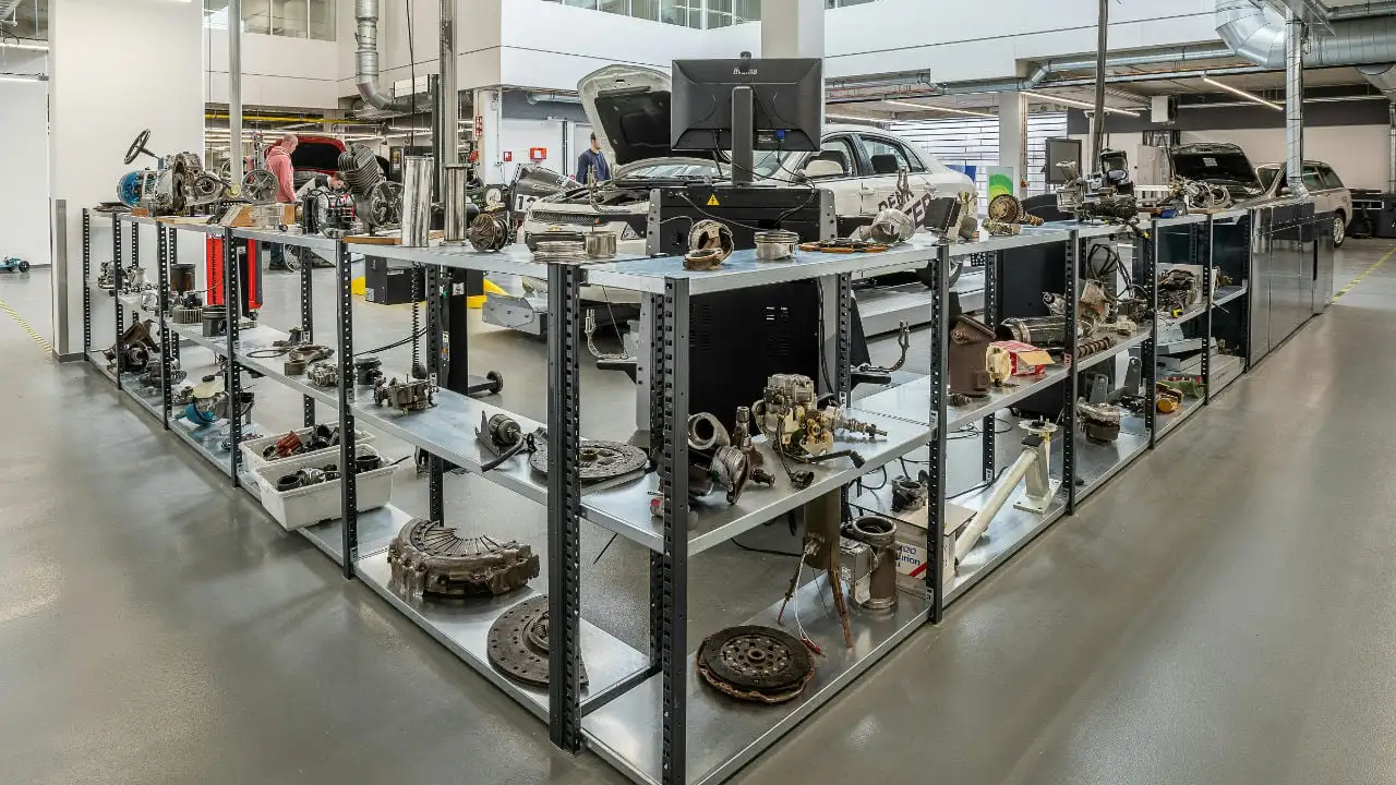 A wide view of a modern auto workshop with shelves in the foreground neatly organized with various car engine parts and components.