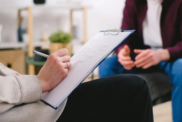 A person in a therapy session with a counselor who is taking notes on a clipboard, representing mental health and addiction treatment.