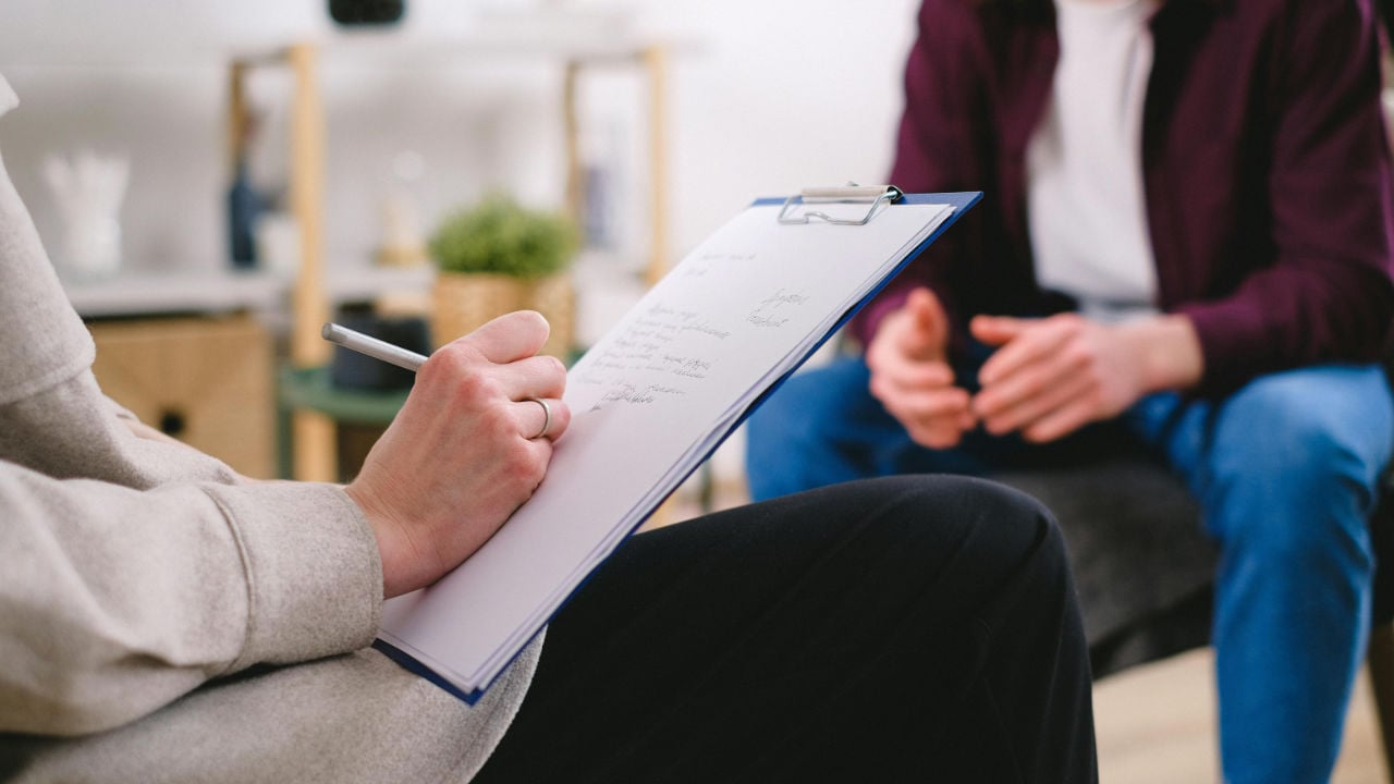 A person in a therapy session with a counselor who is taking notes on a clipboard, representing mental health and addiction treatment.