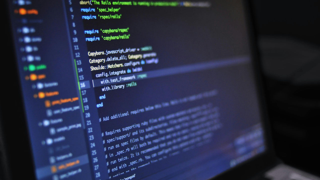 A close-up shot of a laptop screen displaying lines of programming code in a dark room.