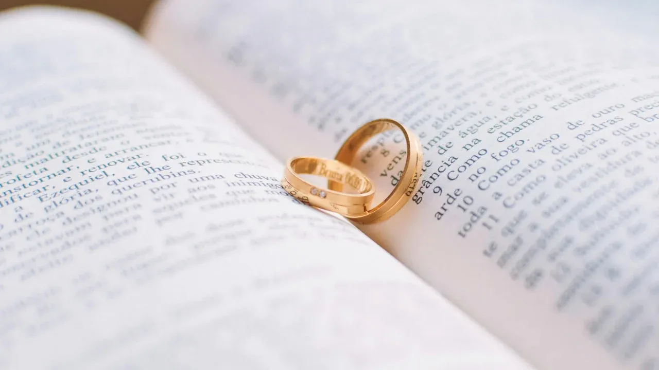 Two gold wedding bands resting on the pages of an open book, with the focus on the rings.