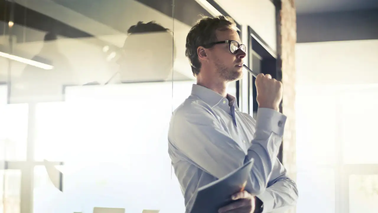A thoughtful businessman looking out a window, contemplating his choice between an E-1 and E-2 visa.