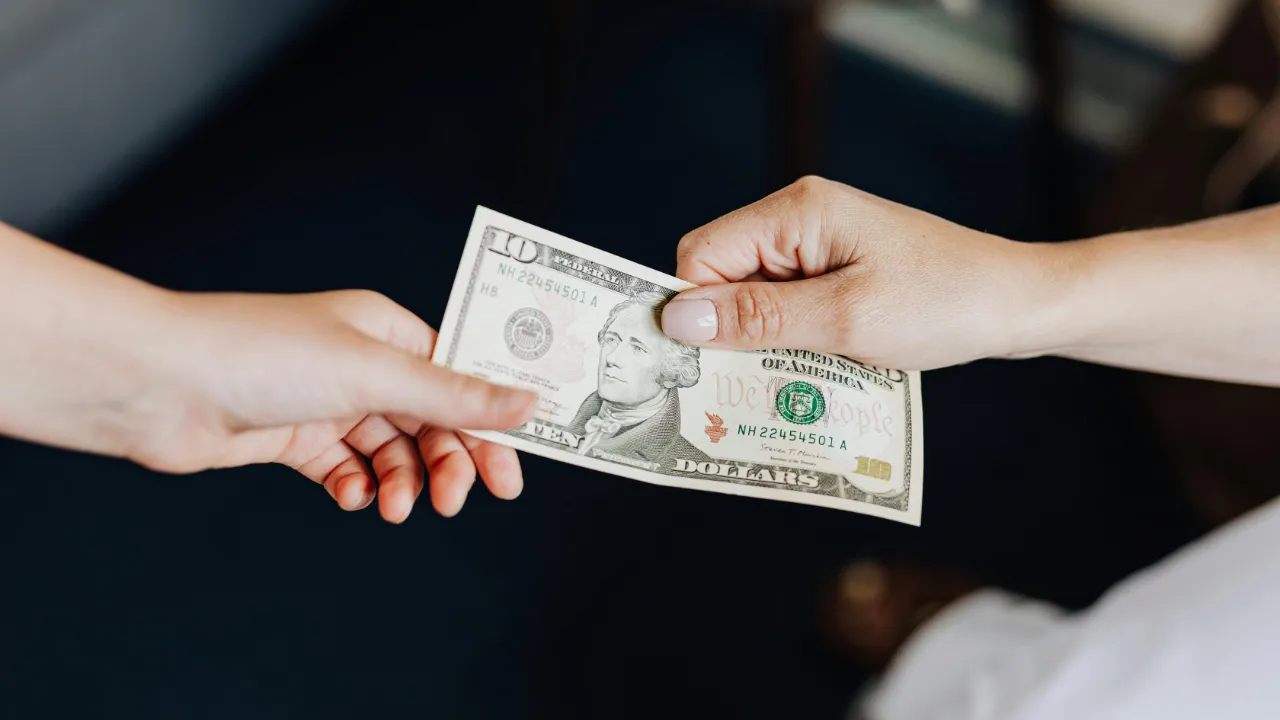 Two hands exchanging a ten-dollar bill, representing a loan for an EB-5 investment.