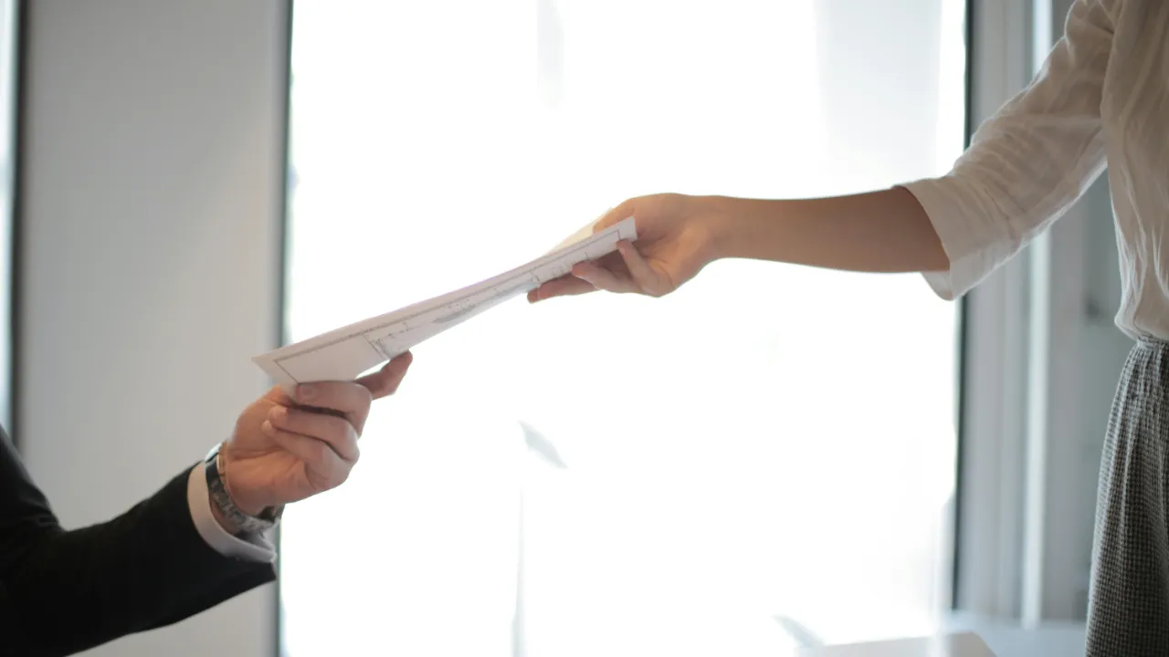 A professional handing a document to another person across a desk, representing a consultation after an E-2 change of status denial.