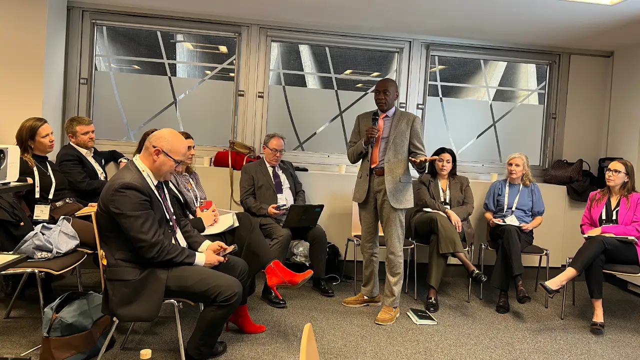 Speaker Ian Scott standing and addressing a panel of seated legal professionals at an international conference.