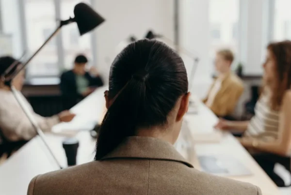 The back of a professional woman's head as she sits in a meeting, representing an employee considering switching jobs while their I-485 is pending.