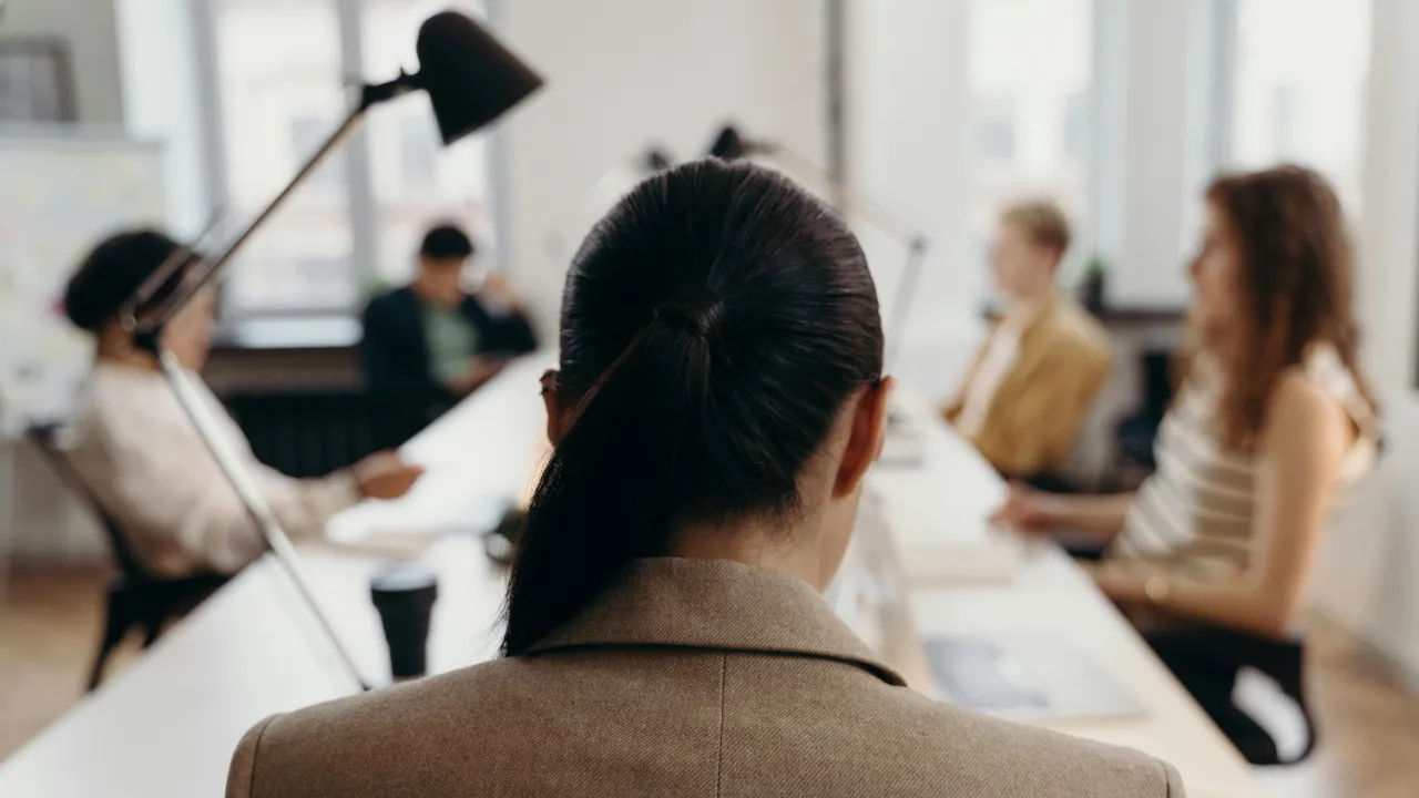 The back of a professional woman's head as she sits in a meeting, representing an employee considering switching jobs while their I-485 is pending.