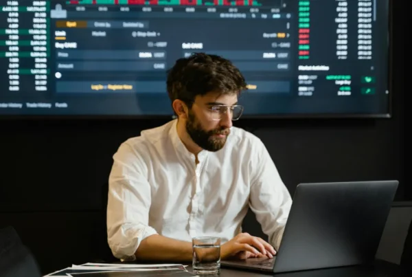 A professional man at a laptop analyzing financial data on a large screen, representing a TN Economist applicant.