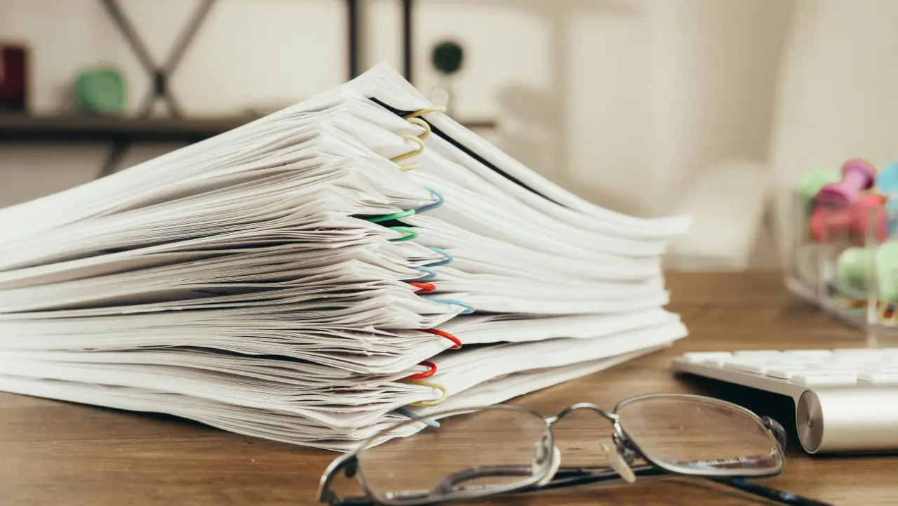 Stack of organised documents with colourful clips on a desk, representing E-2 visa due diligence process.
