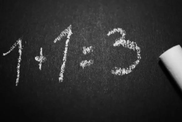 Chalkboard showing incorrect equation “1 + 1 = 3” written in white chalk.