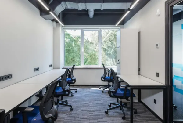 Modern office room with multiple desks and office chairs arranged along both sides of the space.