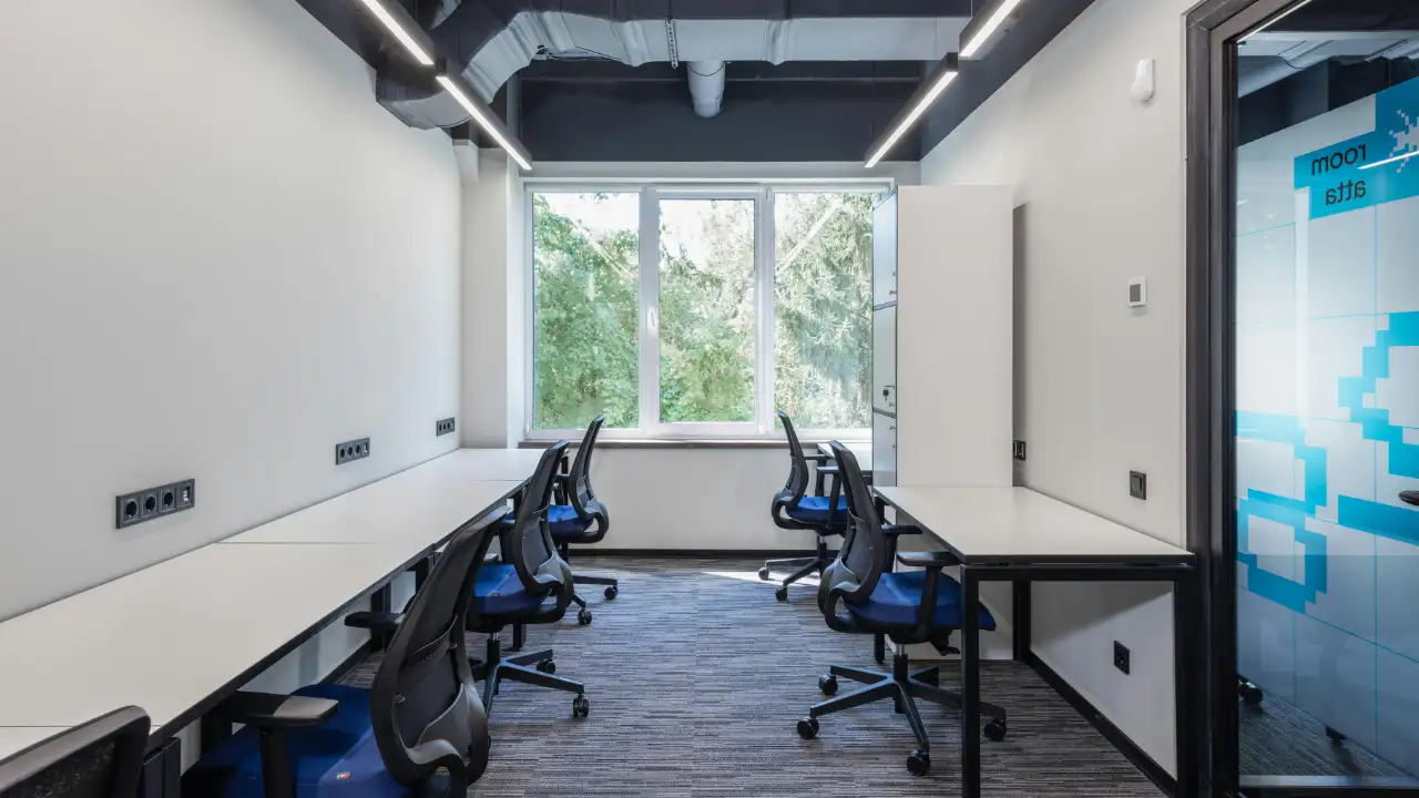 Modern office room with multiple desks and office chairs arranged along both sides of the space.