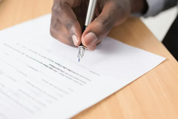 Hand signing an official immigration form with a pen on a wooden desk.