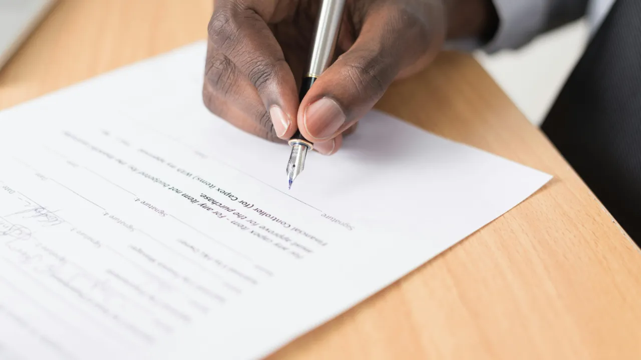 Hand signing an official immigration form with a pen on a wooden desk.