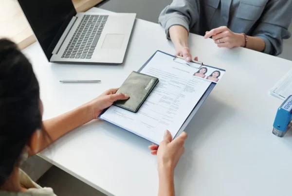 Person submitting passport and visa application documents at a desk during consular processing interview.