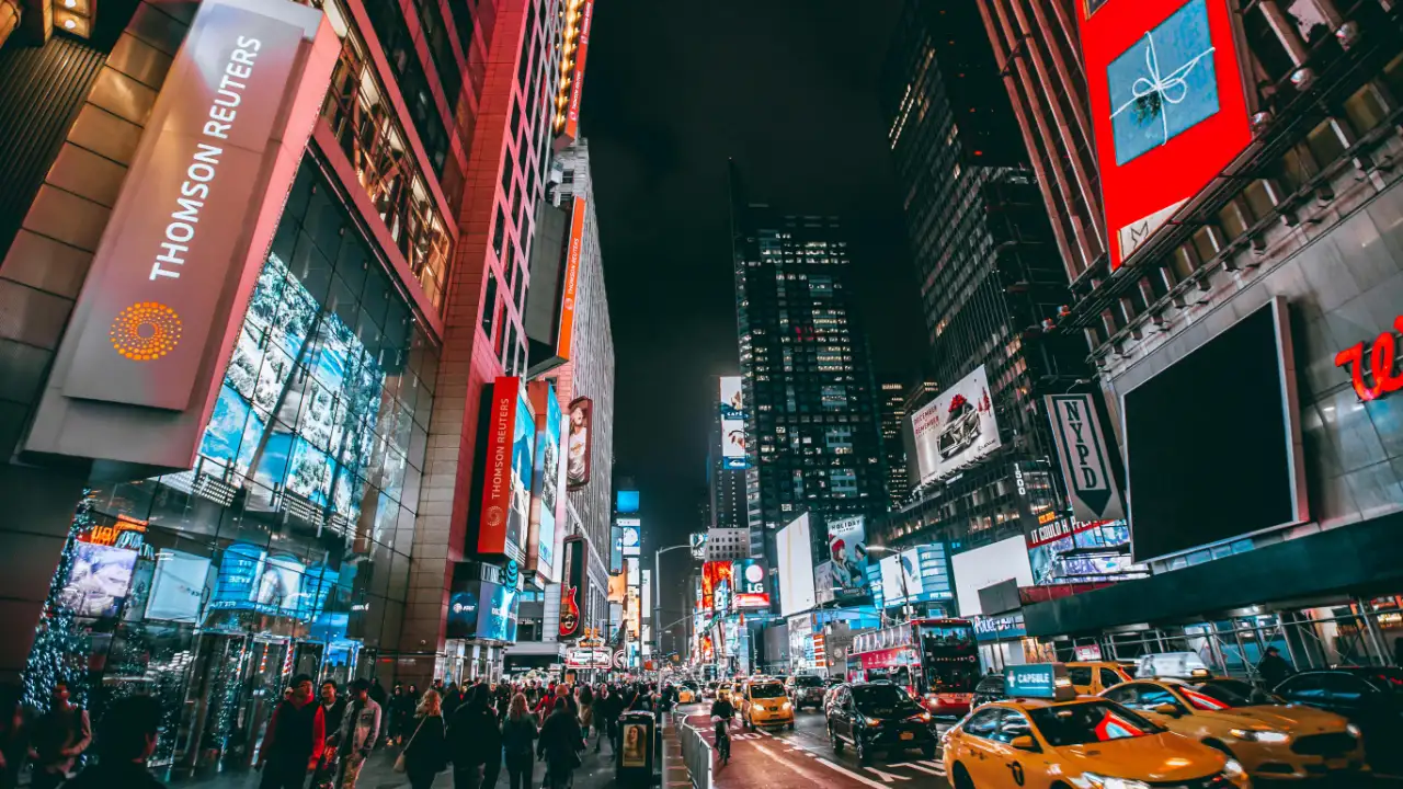 A vibrant night scene of Times Square in New York City with bright billboards, yellow taxis, and busy pedestrians.