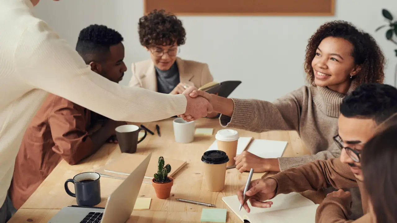A professional group of diverse colleagues shaking hands in a bright, modern office to symbolize a successful employee transfer.