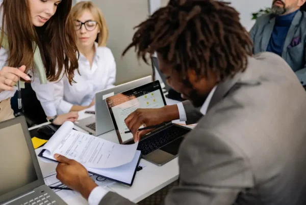 People collaborating in an office while reviewing documents and working on laptops.