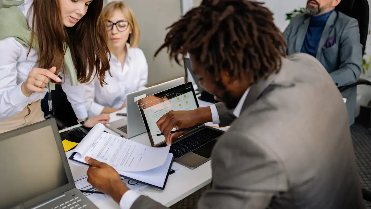 People collaborating in an office while reviewing documents and working on laptops.