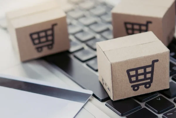 Small cardboard boxes with shopping cart symbols placed on a laptop keyboard next to a credit card.