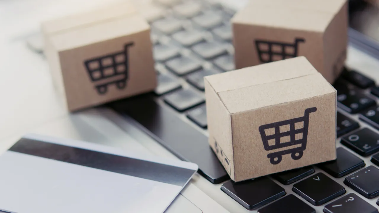 Small cardboard boxes with shopping cart symbols placed on a laptop keyboard next to a credit card.