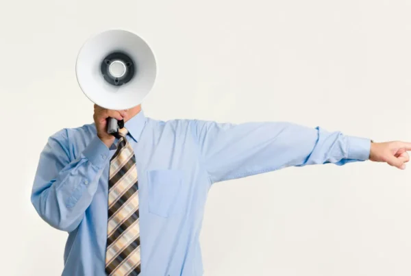 A professional in a blue shirt and tie holding a megaphone and pointing, symbolizing leadership, authority, and the direction of a business enterprise.