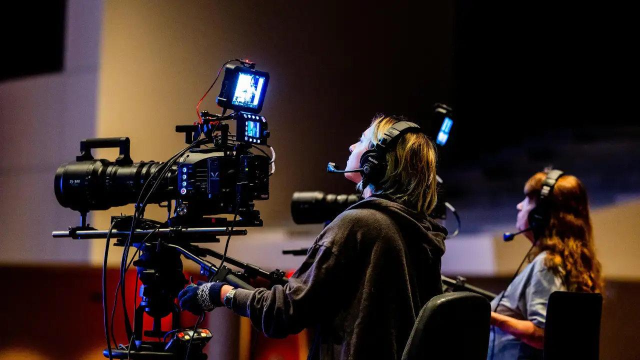 Two camera operators filming with professional video equipment in a studio setting.