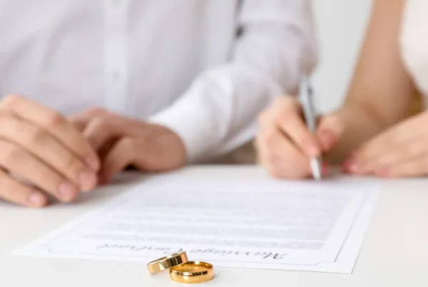 A couple sitting at a table signing a document with two gold rings placed on the paper.