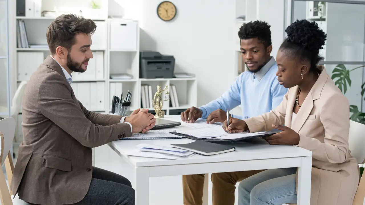 Attorney sitting across two clients at a table reviewing immigration documents.