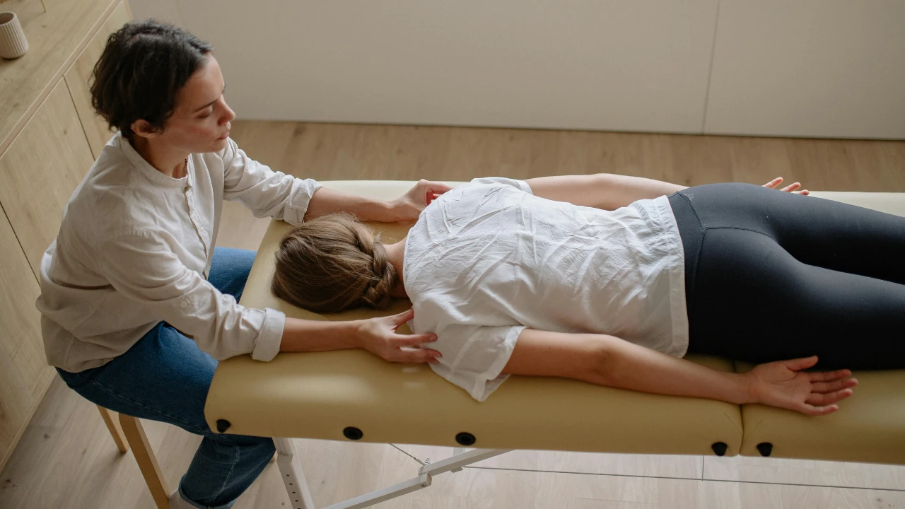 A practitioner providing manual therapy to an individual lying on a treatment table in a clinical room.