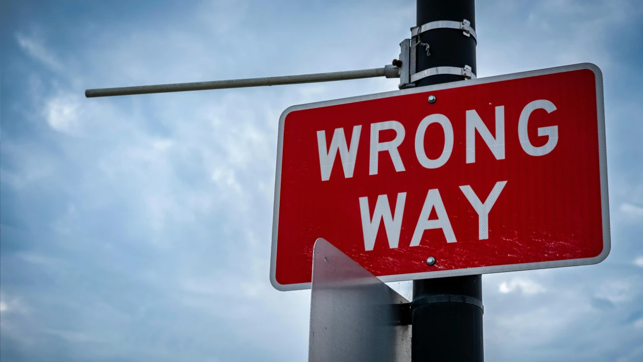 A bright red "WRONG WAY" road sign against a cloudy blue sky, symbolizing high-risk E-2 visa investment approaches.