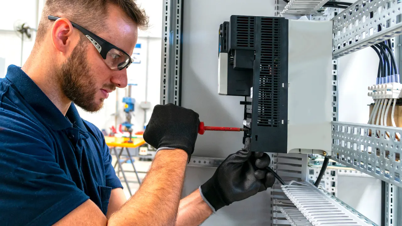 A person wearing gloves and using tools to work on electrical equipment inside a metal panel.