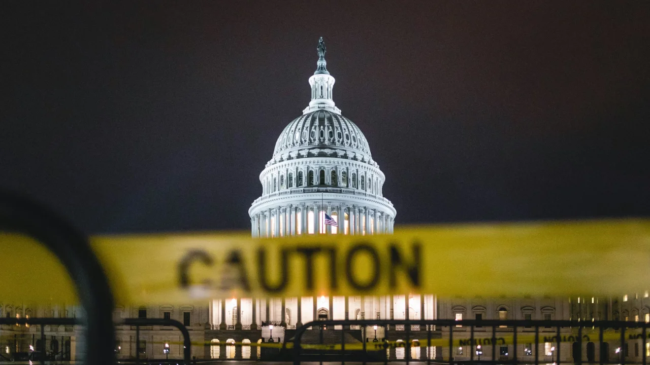 A night view of the illuminated U.S. Capitol dome with a yellow caution tape in the foreground, representing EB-5 Regional Center program deadlines.