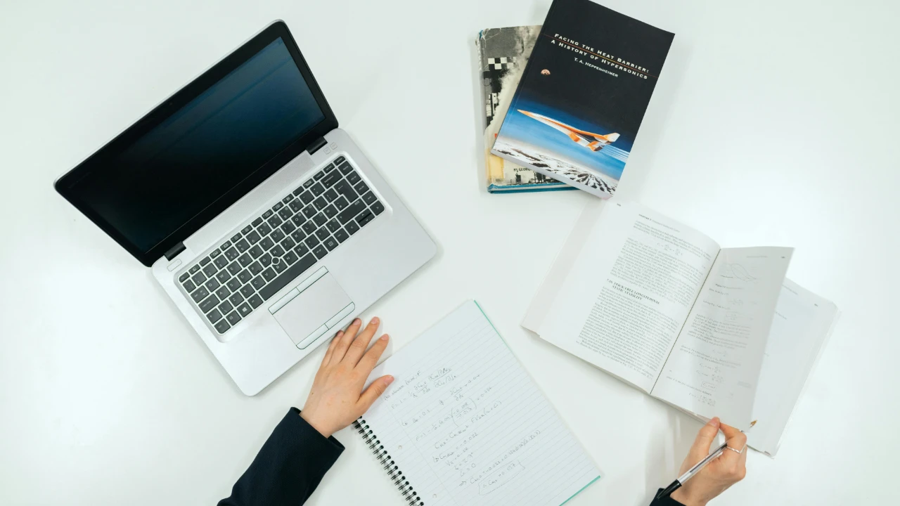 A top-down view of a white desk with a laptop, notebooks, and academic books, symbolizing the research and evidence needed for a strong EB-2 NIW case.