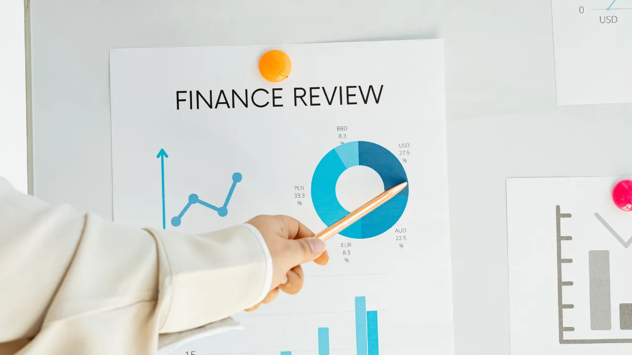 A hand pointing with a pencil to a circular finance chart labeled Finance Review on a whiteboard.