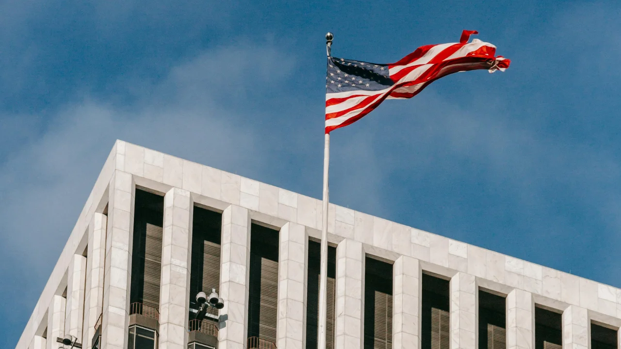 The United States flag waving in front of the U.S. Consulate building in Toronto, Canada, under a blue sky.