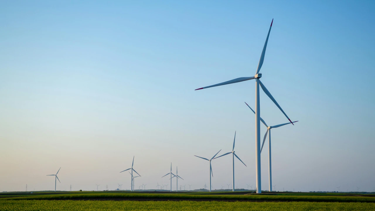 Wind turbines standing in a green field under a clear blue sky.