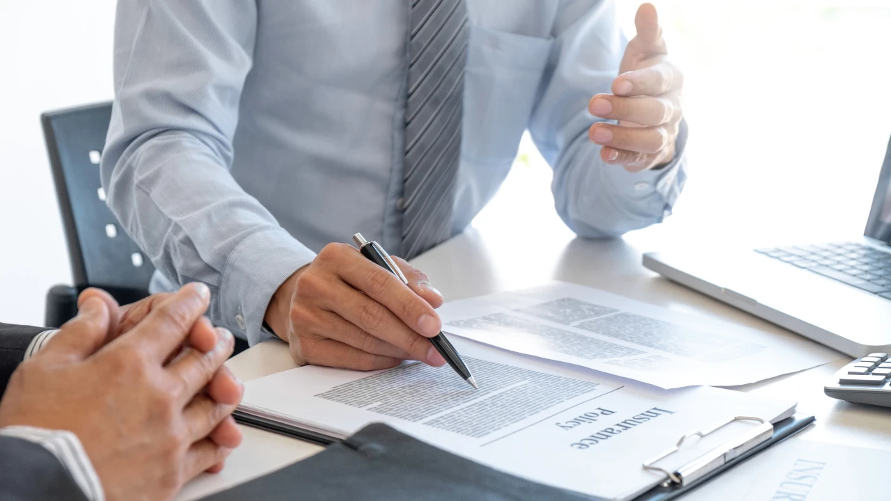 Close-up of hands reviewing and signing documents on a desk during a business meeting.