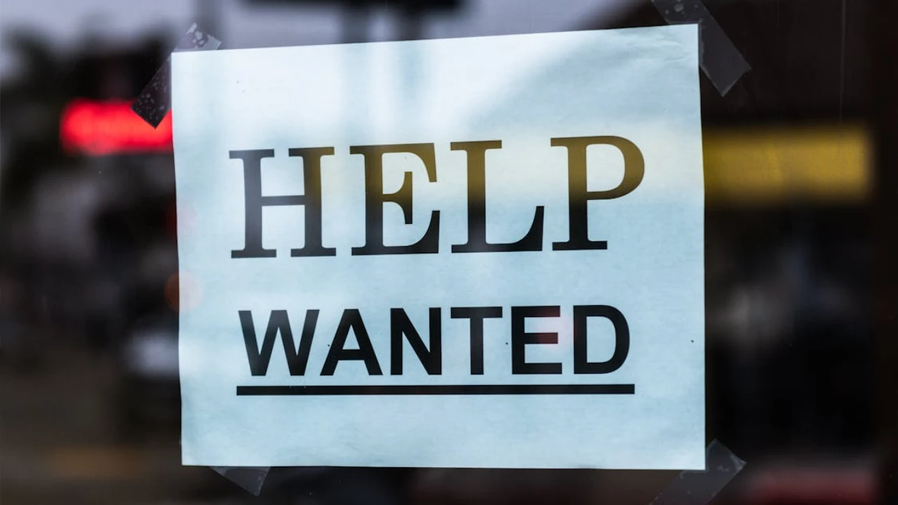 A close-up of a "Help Wanted" sign taped to a window, representing the EB-5 job creation requirement for investors.
