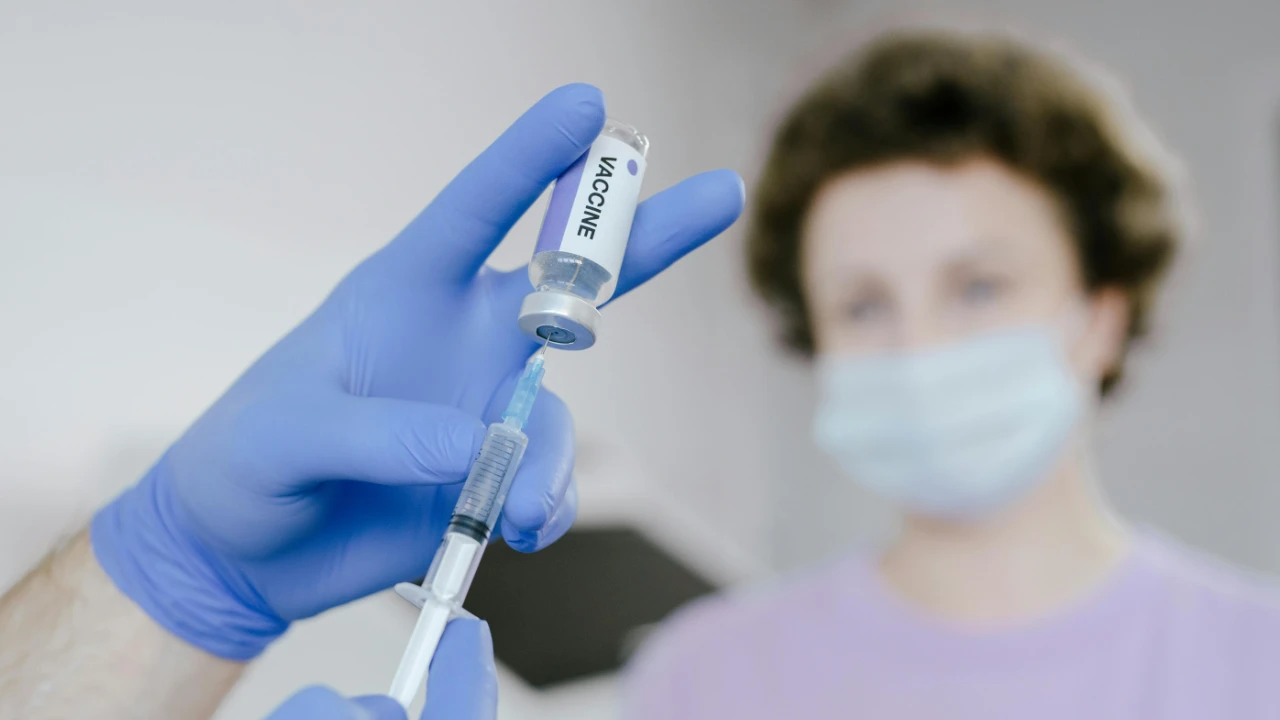 A healthcare professional in blue gloves prepares a vaccine vial for an adjustment of status applicant.