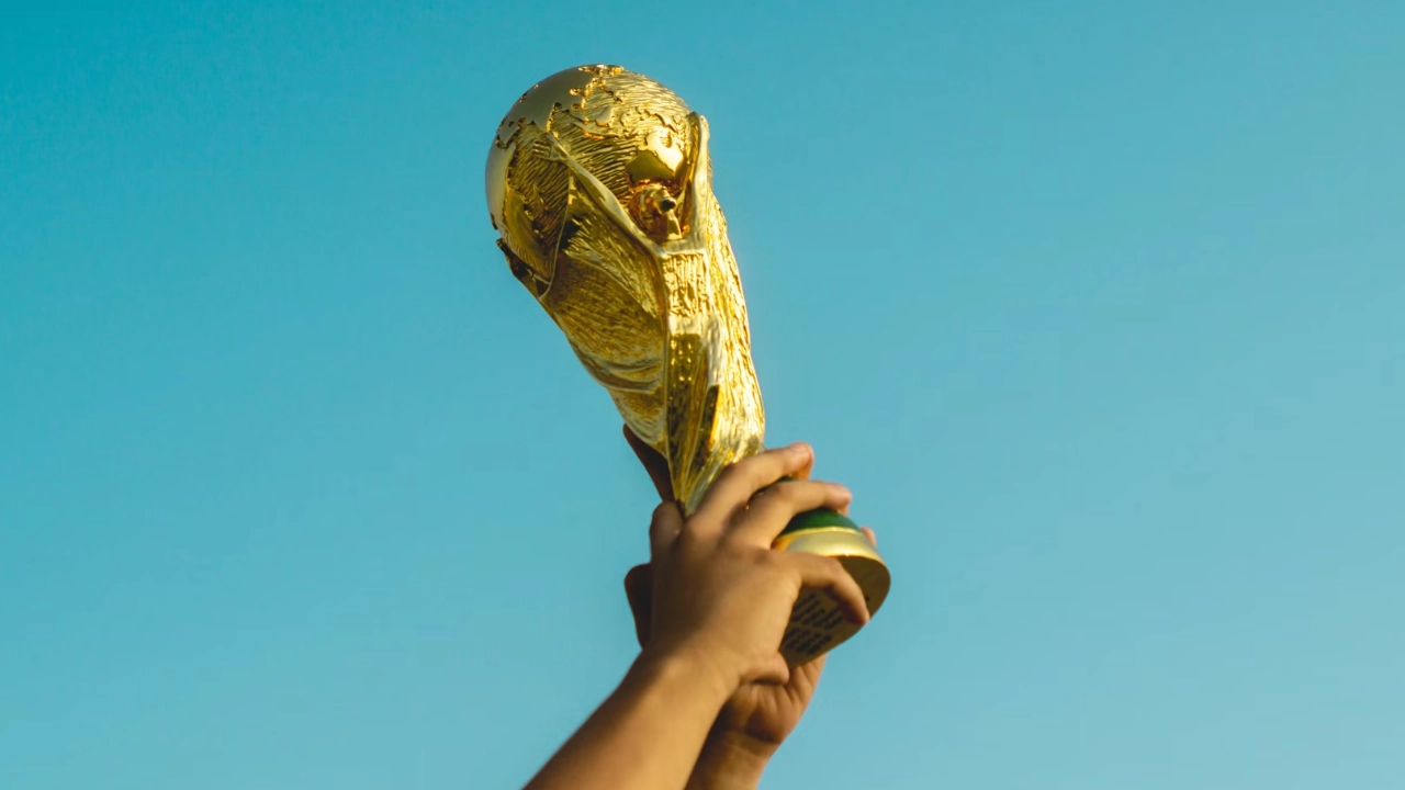Close-up of hands holding the gold FIFA World Cup trophy high against a clear blue sky background.