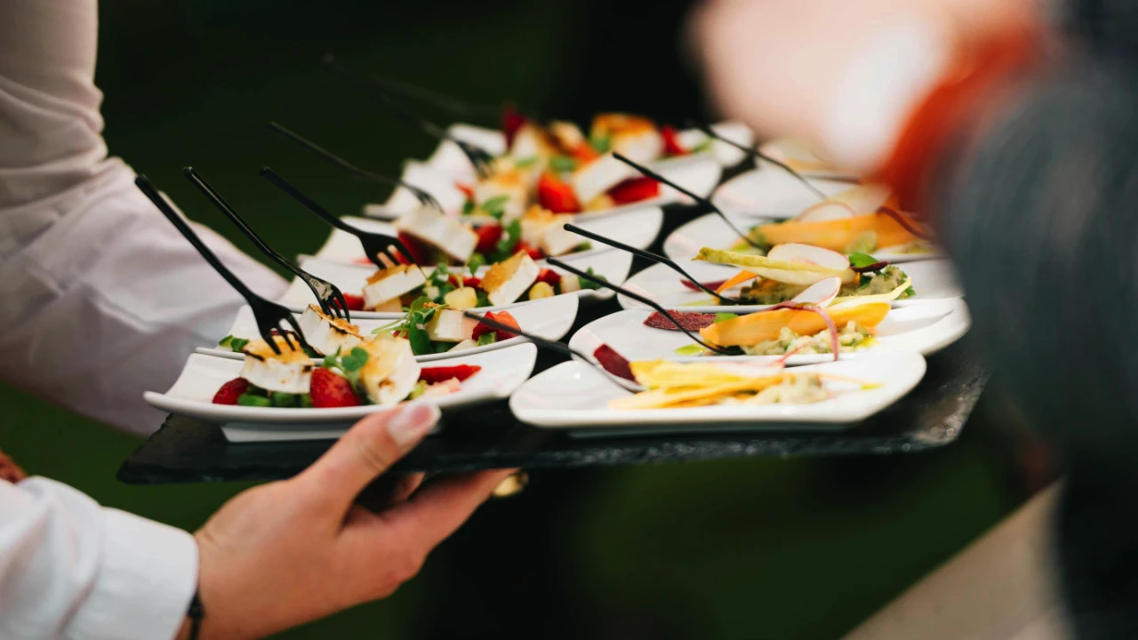 Servers holding trays of plated appetizers with forks at a catered event.