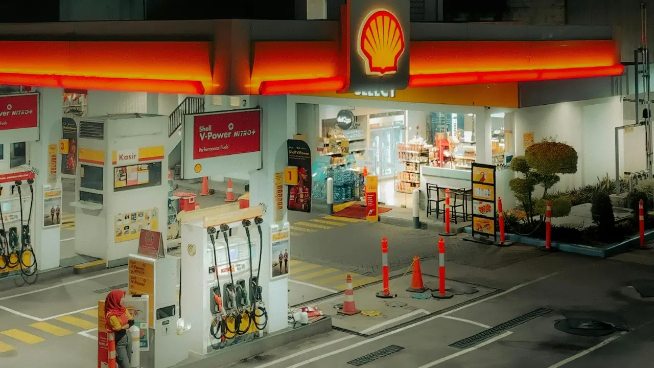Shell gas station and convenience store at night with fuel pumps, bright canopy lighting, and storefront visible.