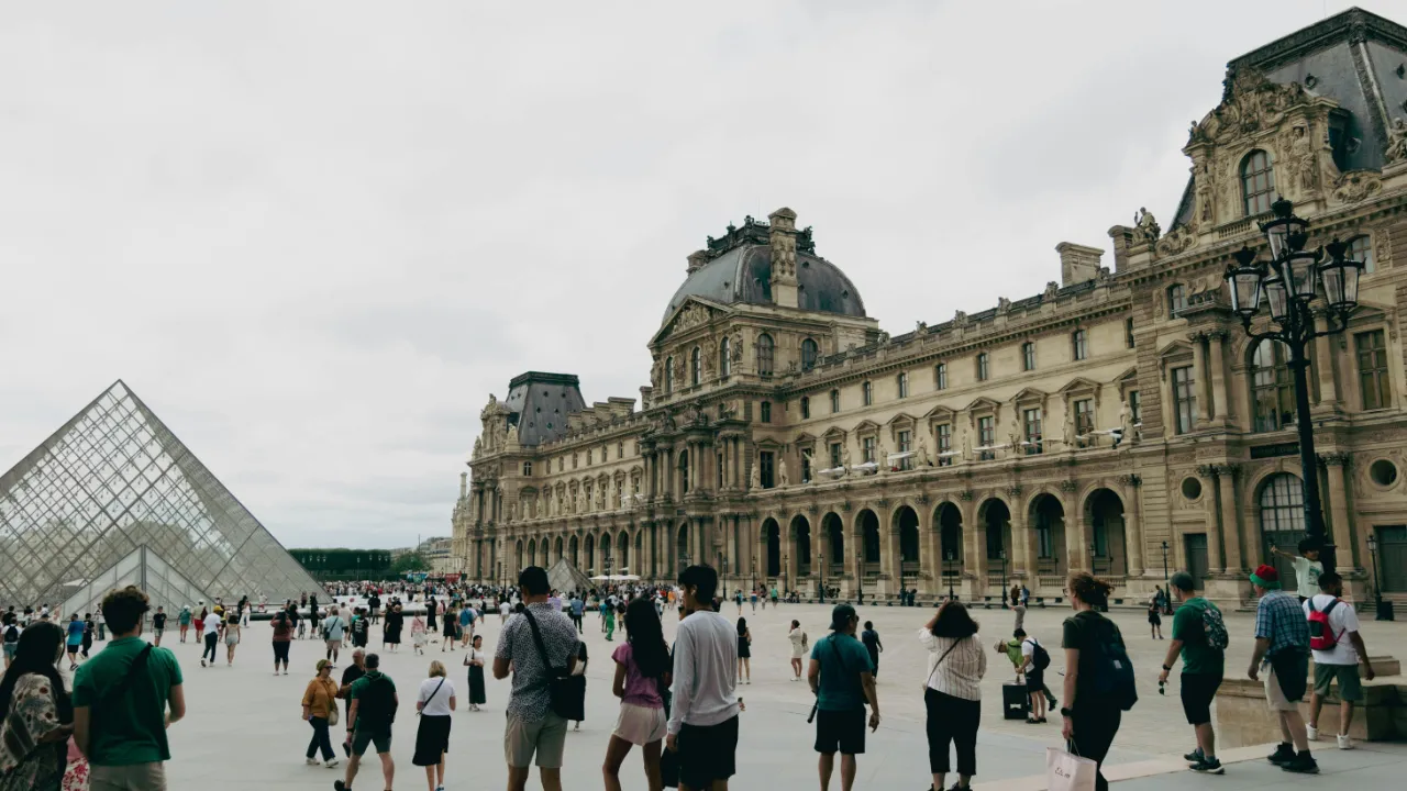 A crowd of diverse tourists walking in the courtyard outside the Louvre Museum in Paris, France, representing international travel.