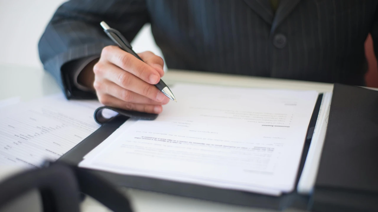 A legal professional's hand signing business incorporation documents for an E-2 visa entity setup.