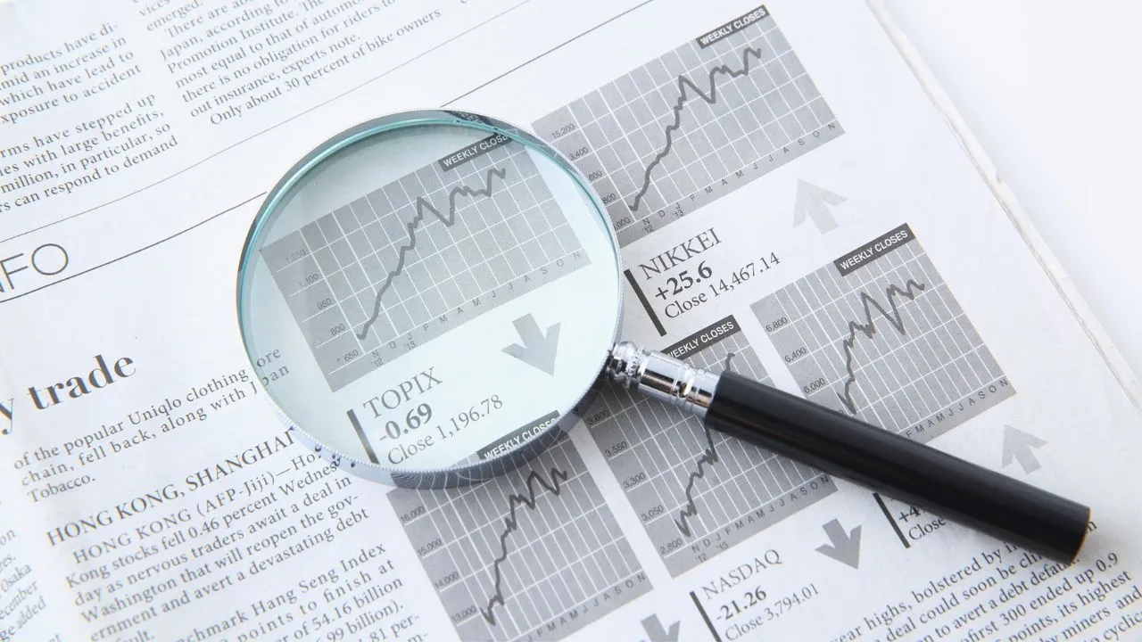 A close-up of a magnifying glass magnifying stock market charts and indices on a financial newspaper page.