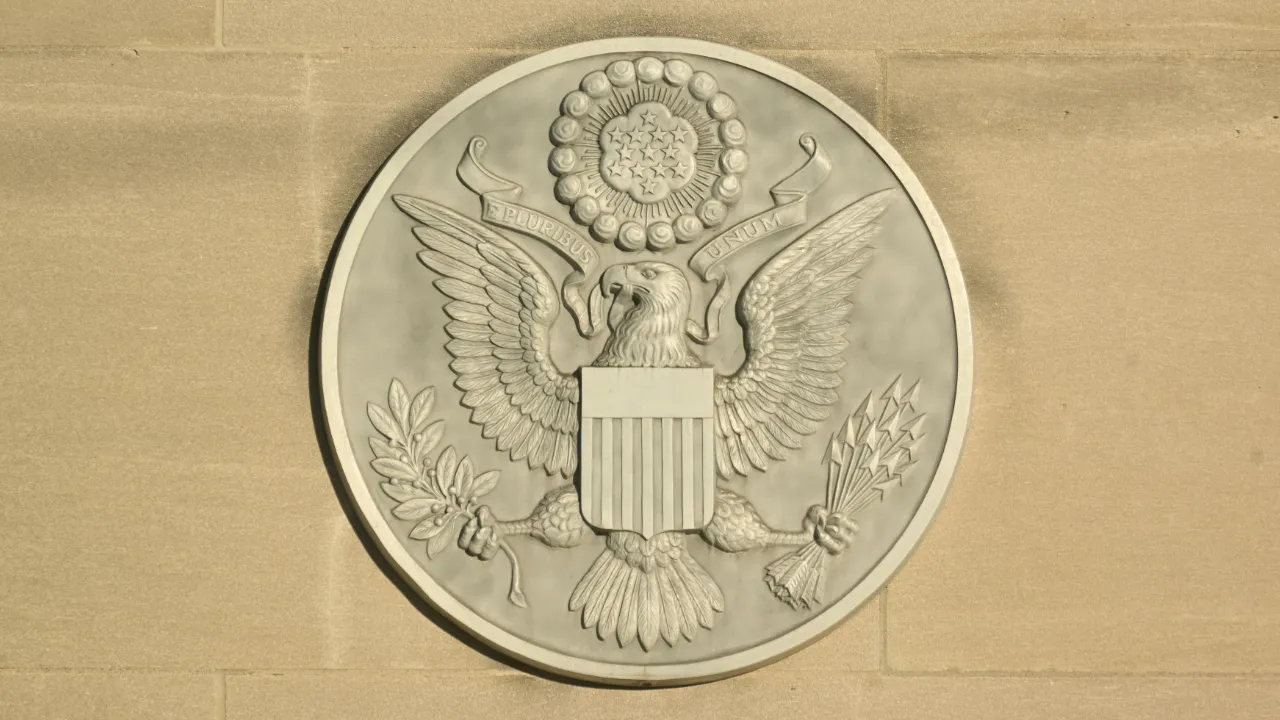 A stone carving of the Great Seal of the United States on an exterior wall, representing official USCIS adjustment of status policies.