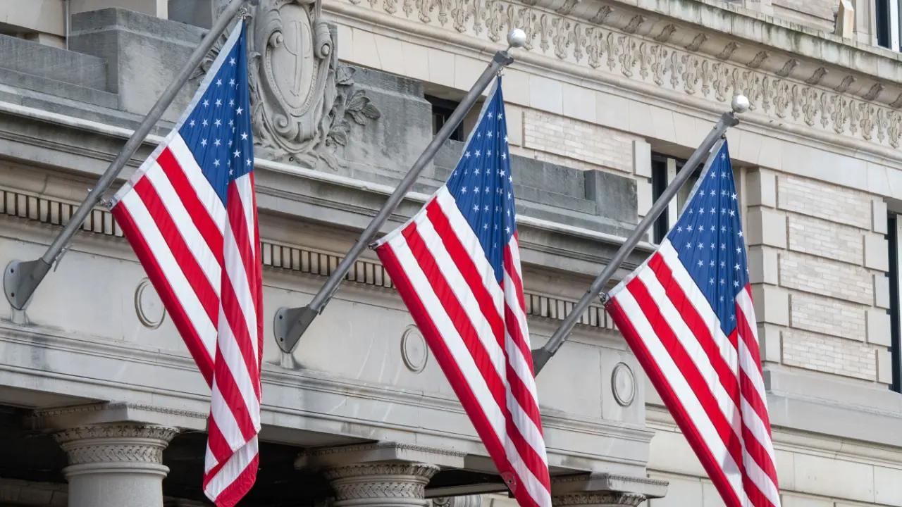 Three American flags flying on the stone facade of a classical-style federal government building, representing USCIS and US immigration offices.