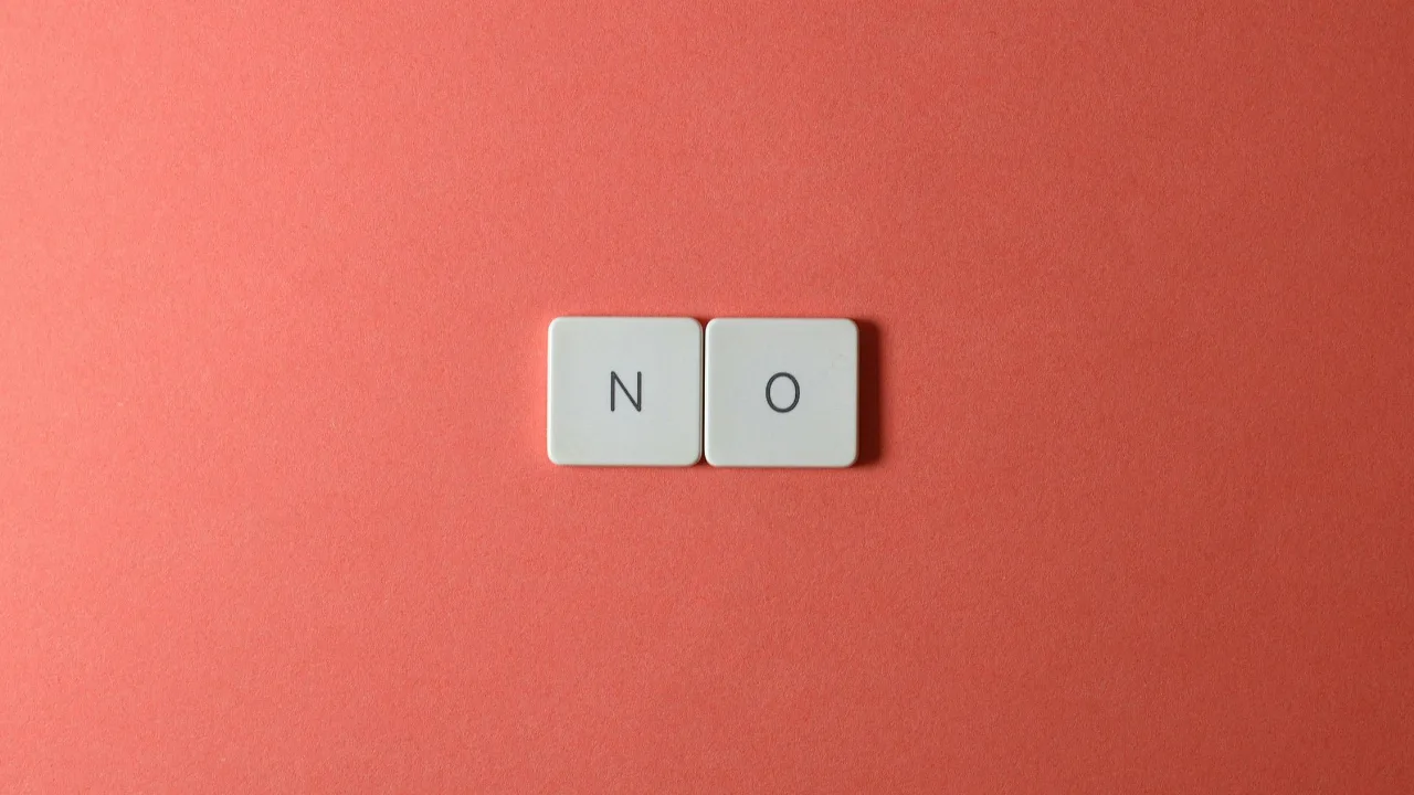 Two white tiles spelling the word 'NO' centered on a solid coral-colored background, representing a USCIS application rejection.