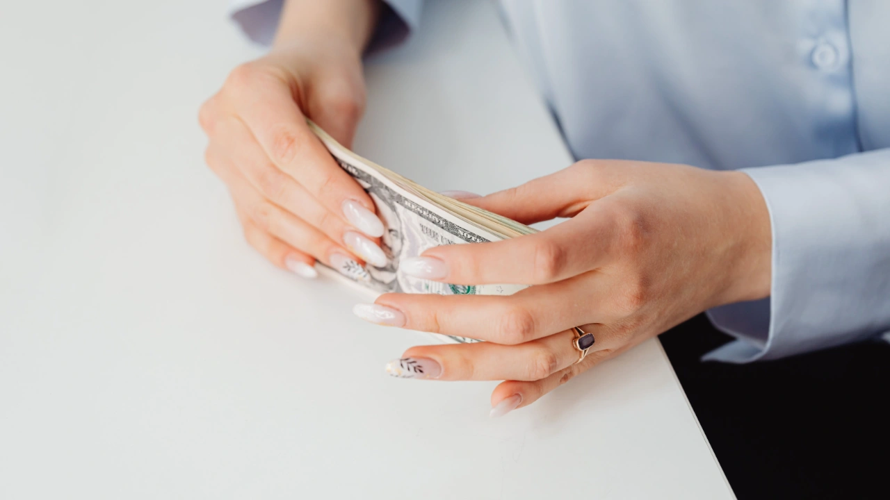 Close-up of a professional's hands counting a stack of US dollar bills on a white desk, representing an employer's financial ability to pay the offered wage.